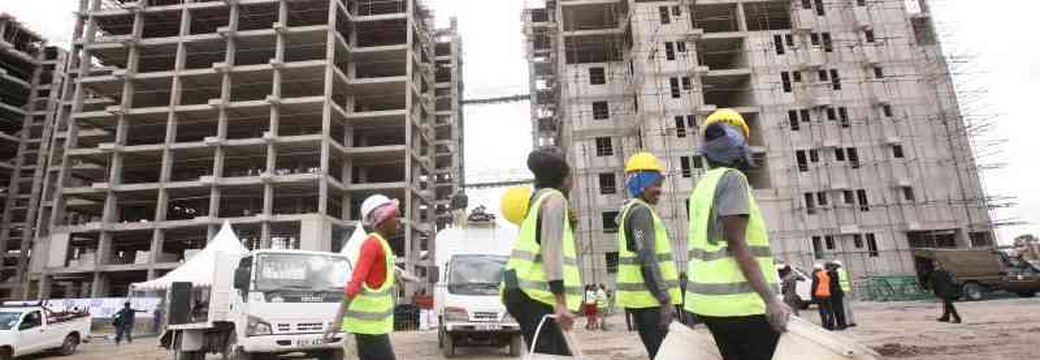 Workers in high-visibility vests carrying buckets at an affordable housing construction site in Kenya
